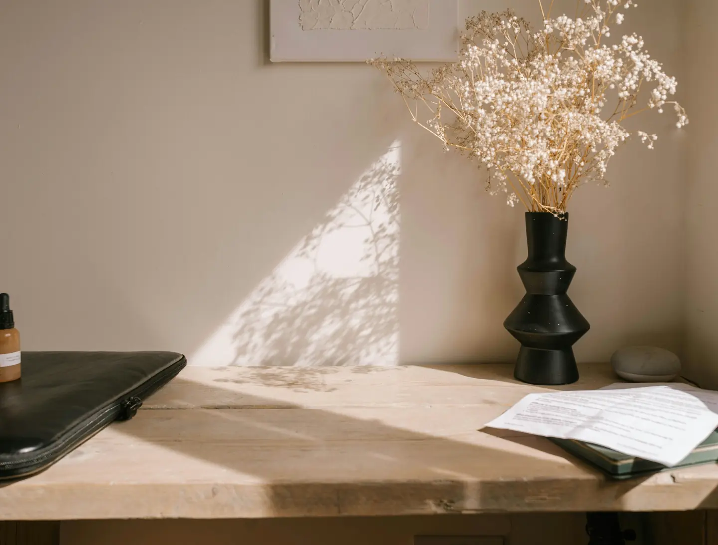 A calm, sunlit workspace with dried flowers in a vase